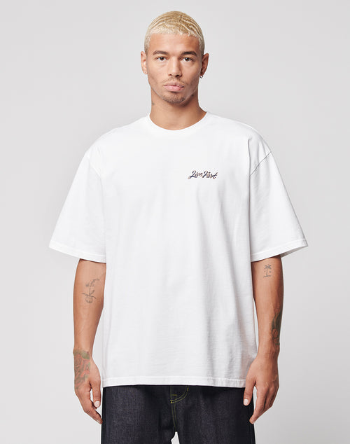 A man with short, bleached blond hair wears the LIVE FAST DIE YOUNG LFDY Westend Tee in oversize fit with Low Poly on the chest and a backprint, paired with dark jeans, standing against a light gray background. Made from 100% Baumwolle.