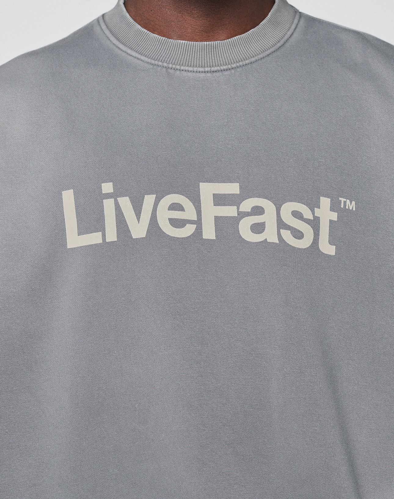 Close-up of the Basic LiveFast Sweater by LIVE FAST DIE YOUNG, a grey sweatshirt with a faded finish and bold white "LiveFast" lettering alongside a small TM symbol.