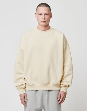 A person with short hair wears the LIVE FAST DIE YOUNG Basic Blank Sweater in light beige with a loose, oversize fit and soft Baumwolle, paired with light gray pants and standing against a plain white background.