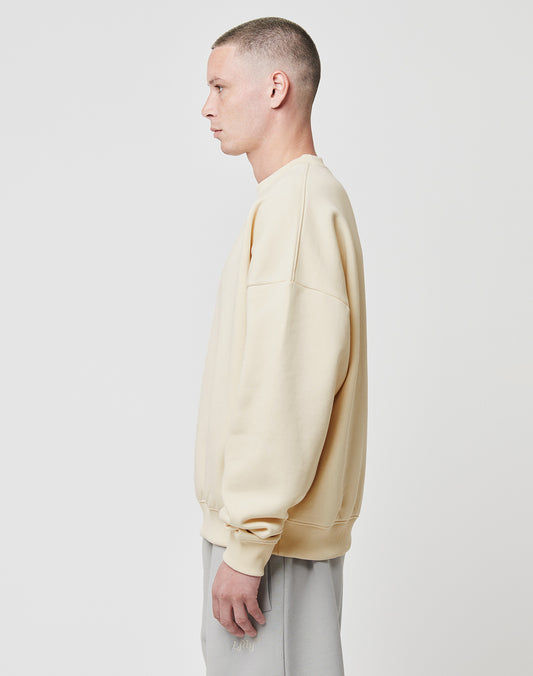 A person with short hair faces left, wearing the LIVE FAST DIE YOUNG Basic Blank Sweater in beige and light gray pants, standing against a plain white background.