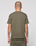 A person with short hair and visible tattoos stands facing away, wearing the LIVE FAST DIE YOUNG Live Fast Rhinestone Tee in olive green and matching shorts against a plain light background.