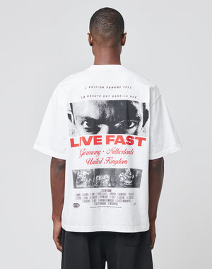 A person wears the LFDY Cinema Tee by LIVE FAST DIE YOUNG—an oversized white cotton T-shirt with a black-and-white face print, bold red LIVE FAST text, and detailed back design, photographed from behind on a plain background.