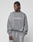 A person with braided hair looks to the side, wearing the gray Basic LiveFast Sweater by LIVE FAST DIE YOUNG with handgefertigtem Fade-Effekt and Oversize Fit, paired with matching sweatpants, against a plain light background.