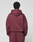 A person with short curly hair faces away, wearing a maroon LIVE FAST DIE YOUNG Basic Hooded Zip and matching sweatpants in an oversize fit, against a plain light gray background.