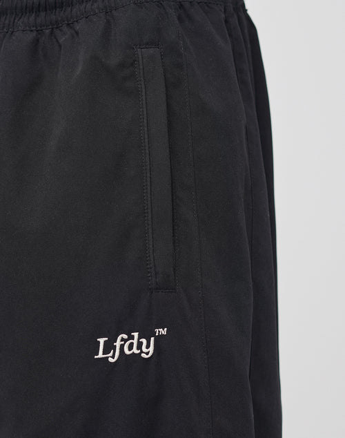 The LFDY Trackpants by LIVE FAST DIE YOUNG are black polyester pants with an elastic waistband, a zippered vertical side pocket, and white LFDY™ embroidery near the pocket. They feature a regular fit and are shown against a light background.