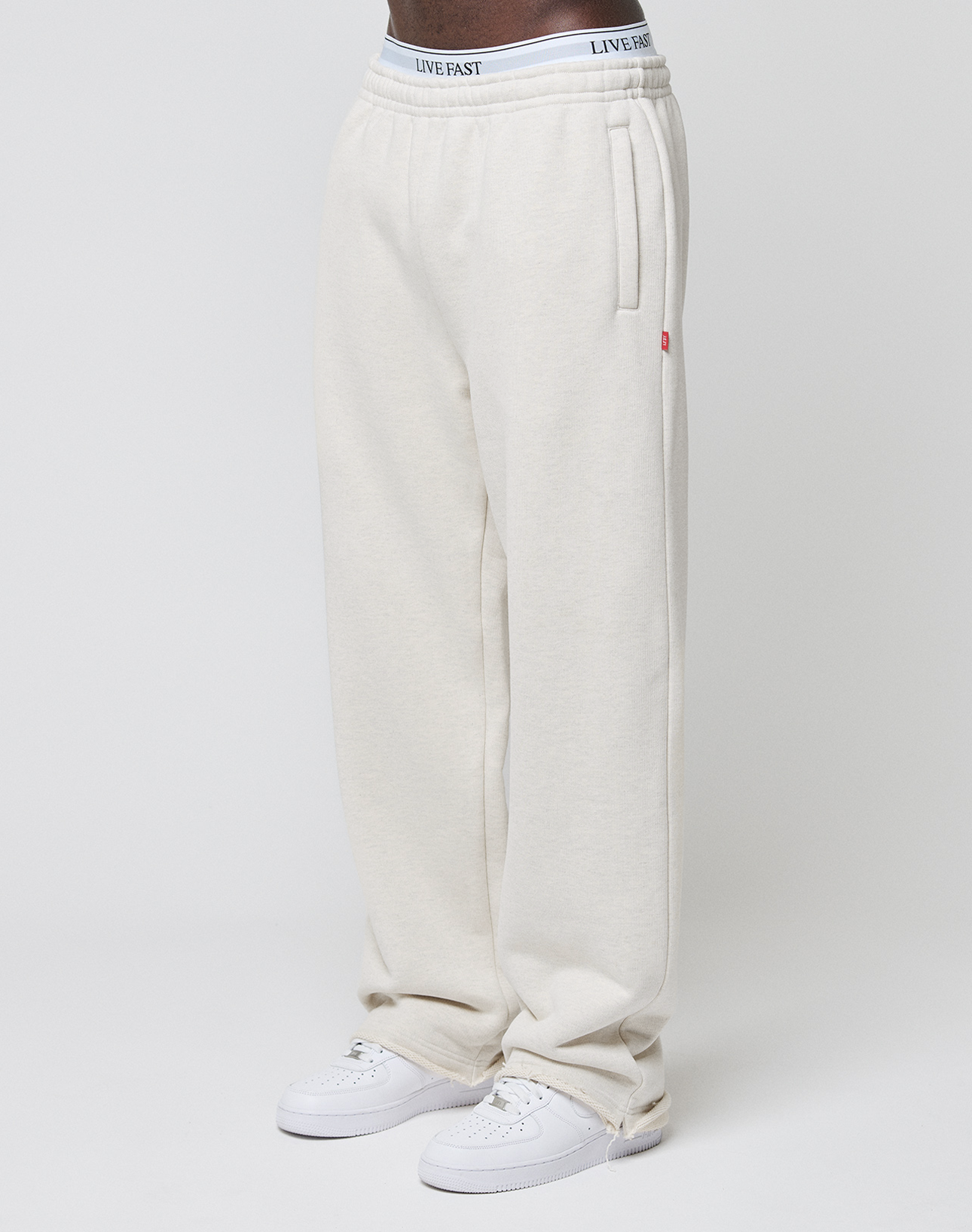 A person wears off-white LFDY Heavyweight Loungepants by LIVE FAST DIE YOUNG, made from 650gsm cotton with a drawstring and elastic waistband featuring "LIVE FAST" text, paired with white sneakers against a plain light background.