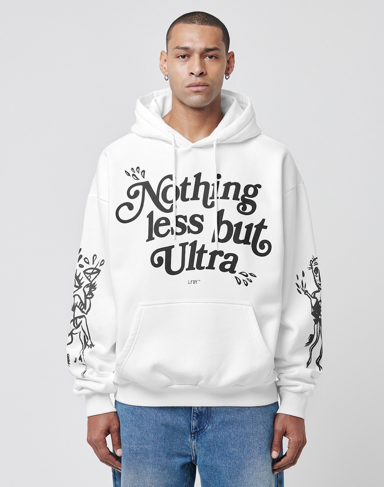 A person wearing the LFDY Ultra Hooded by LIVE FAST DIE YOUNG, featuring "Nothing less but Ultra" in bold black letters on the front and black graphics on both sleeves with Bündchen an Ärmeln, stands against a plain light background.