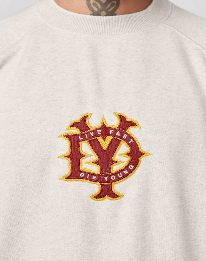 A close-up of the light gray DY Sweater by LIVE FAST DIE YOUNG shows topstitching and a red and yellow embroidered brand emblem in a stylized design. The wearers tattooed neck is visible above the collar.