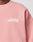 Close-up of the Basic Chest Sweater by LIVE FAST DIE YOUNG, a light pink oversized sweatshirt with white Live Fast Die Young text on the front left. Plain background, with part of a persons neck and chin visible.