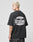 A person with short blond hair, dressed in the LIVE FAST DIE YOUNG LFDY Bulge Tee—an oversized black cotton shirt with a large white Everybody Livefast Eats backprint—stands sideways facing left against a plain light gray background.