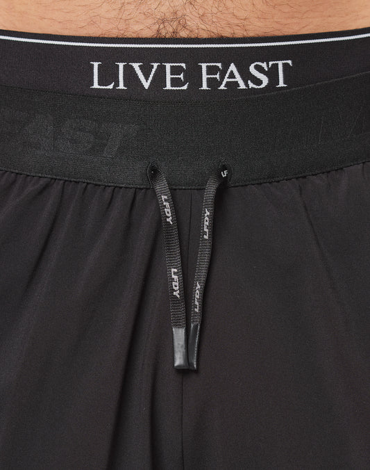 Close-up of a waist wearing LIVE FAST DIE YOUNGs Live Fast Performance Shorts in black, featuring an elastic waistband with LIVE FAST lettering and black drawstrings with white text. Regular Fit offers comfort and style.