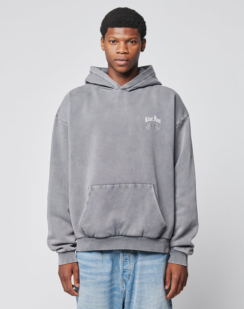 A young man faces forward, wearing the LFDY Haters Hooded by LIVE FAST DIE YOUNG—an oversized gray cotton hoodie with hood, front pocket, and small white text and graphic on the left chest. He pairs it with light blue jeans against a light gray background.