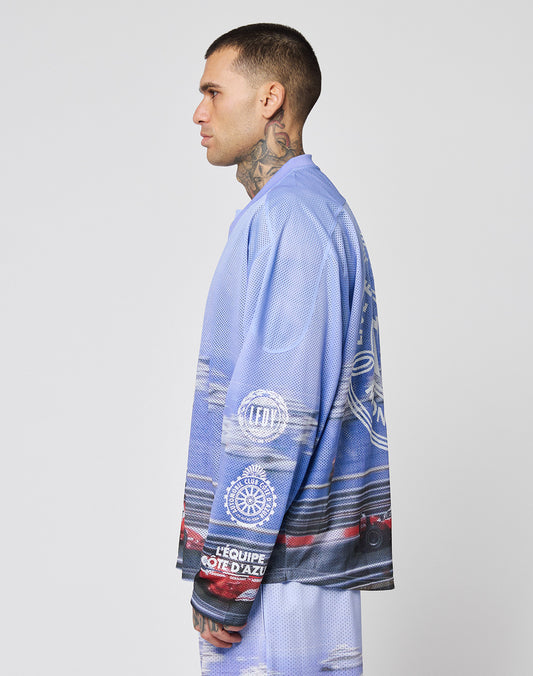 A man with short hair and tattoos on his neck and hand stands in profile, wearing the LIVE FAST DIE YOUNG LFDY Yacht Jersey—an oversize blue and purple 100% polyester graphic shirt with matching logo shorts.