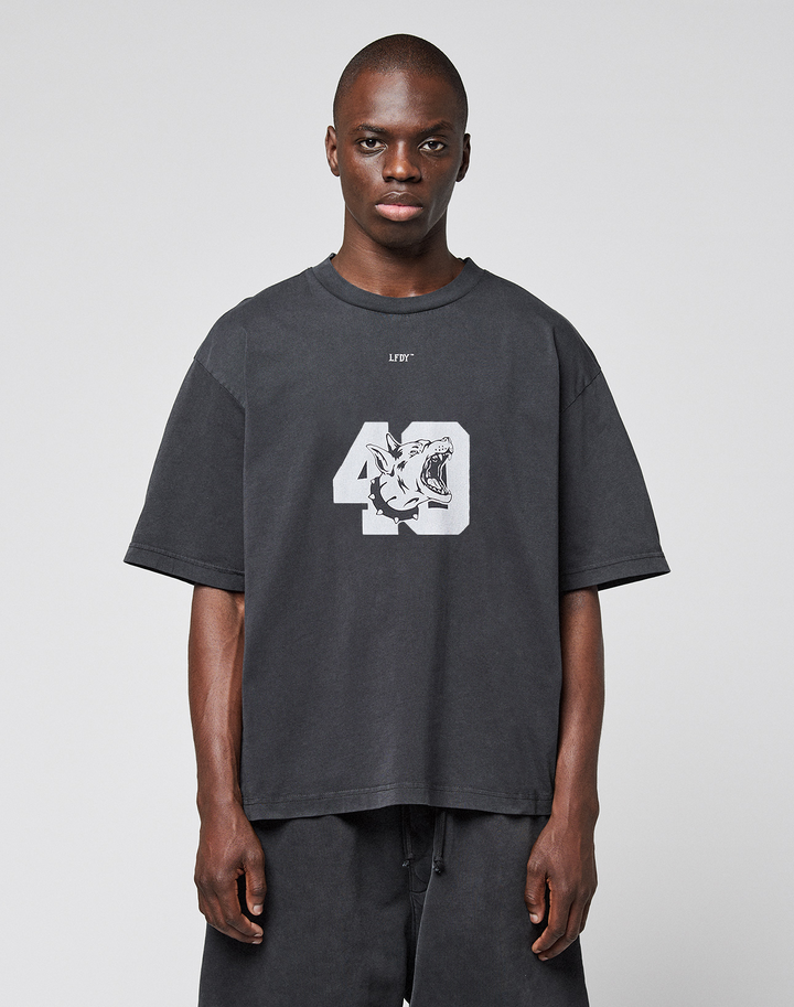 A man faces forward wearing the LIVE FAST DIE YOUNG LFDY 40 Tee—an oversized black T-shirt made of 100% Baumwolle with a bold front print featuring the number 49 and a tiger graphic—paired with black shorts against a light gray backdrop.