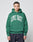 A person faces forward in an oversize fit, green LIVE FAST DIE YOUNG Live Fast College Hooded sweatshirt made from Baumwolle with a bold LIVE FAST frontprint, paired with dark jeans against a plain light background.