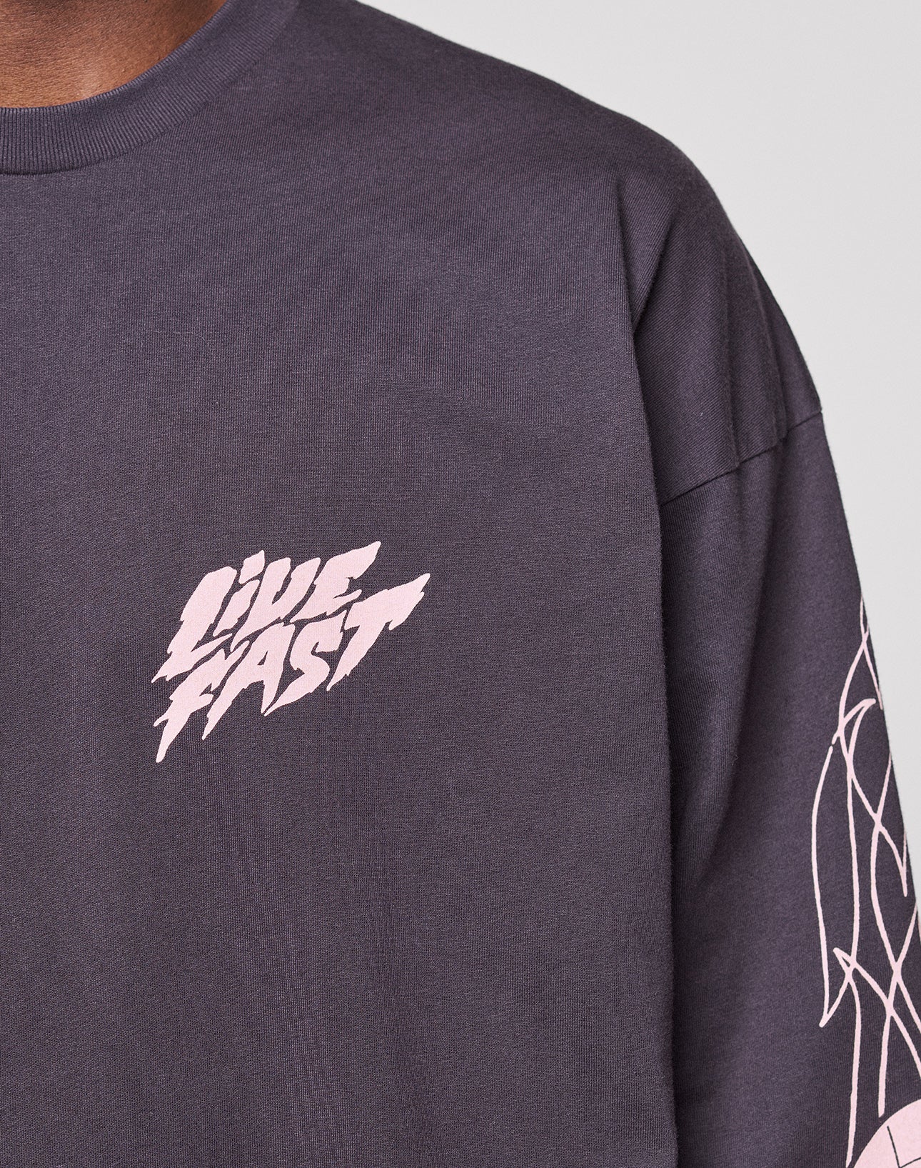 Close-up of a person in an oversize fit LFDY Logo Longsleeve by LIVE FAST DIE YOUNG, featuring bold "LIVE FAST" text on the chest, abstract light sleeve designs, and crafted from 100% Baumwolle.