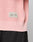 A close-up of the LFDY Knit Sweater by LIVE FAST DIE YOUNG in light pink, with a fabric label and trendy dropped shoulders, worn above black pants and featuring an oversized fit.