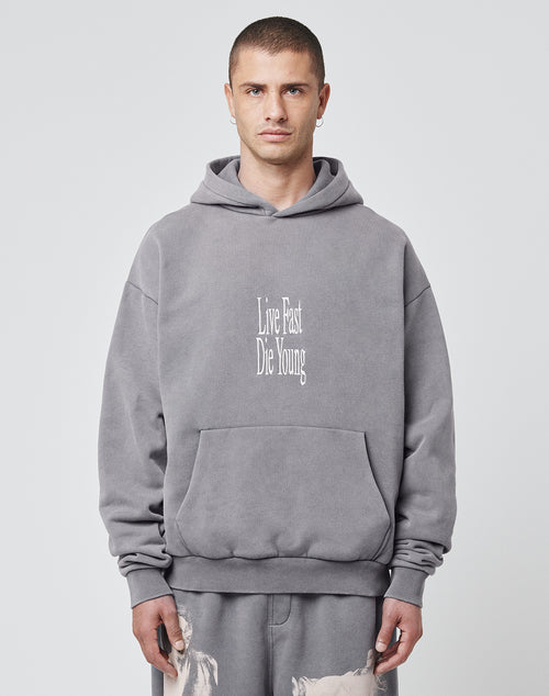 A person wearing the LFDY Stitched Hooded by LIVE FAST DIE YOUNG, an oversize gray hoodie made from a soft cotton-polyester blend with Live Fast Die Young in white on the front, stands against a plain light background.