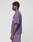 A person stands in profile against a plain background, wearing the LIVE FAST DIE YOUNG Basic OS Livefast Tee in oversize fit purple 100% Baumwolle with a pink frontprint, paired with matching purple shorts.