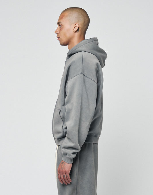 A man with a shaved head stands in profile, facing left, wearing the LIVE FAST DIE YOUNG Basic Hooded Zip and matching sweatpants in faded gray with subtle distressing, set against a plain white background.