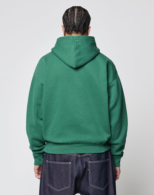 A person with braided hair is seen from behind, wearing the LIVE FAST DIE YOUNG Live Fast College Hooded sweatshirt with a bold backprint and dark denim jeans, standing against a plain light backdrop.