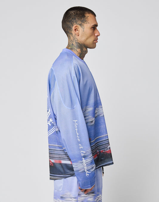 A man with a buzz cut and neck tattoos stands in profile wearing the LIVE FAST DIE YOUNG LFDY Yacht Jersey—an oversize blue and purple graphic long-sleeve shirt with matching shorts, white script on the sleeve—set against a plain light gray background.
