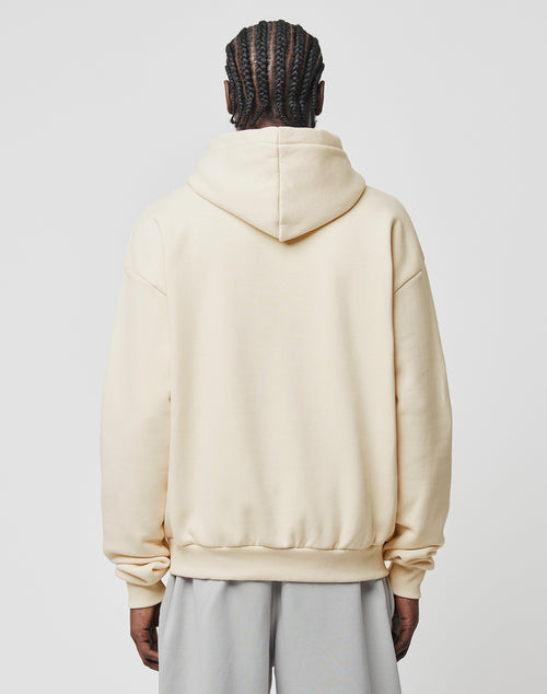 A person with cornrow braids, seen from the back, wears an oversize fit Basic Blank Hooded by LIVE FAST DIE YOUNG in light beige and light gray pants, set against a plain white background.