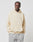 A person in a LIVE FAST DIE YOUNG Basic Blank Hooded, oversize fit, light beige Baumwolle-Polyester blend hoodie with hands in the front pocket, and light gray pants stands against a plain white background.