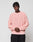 Wearing the LIVE FAST DIE YOUNG LFDY Knit Sweater in light pink with an oversized, ribbed design and paired with black pants, a person stands against a plain light gray background with hands clasped in front.