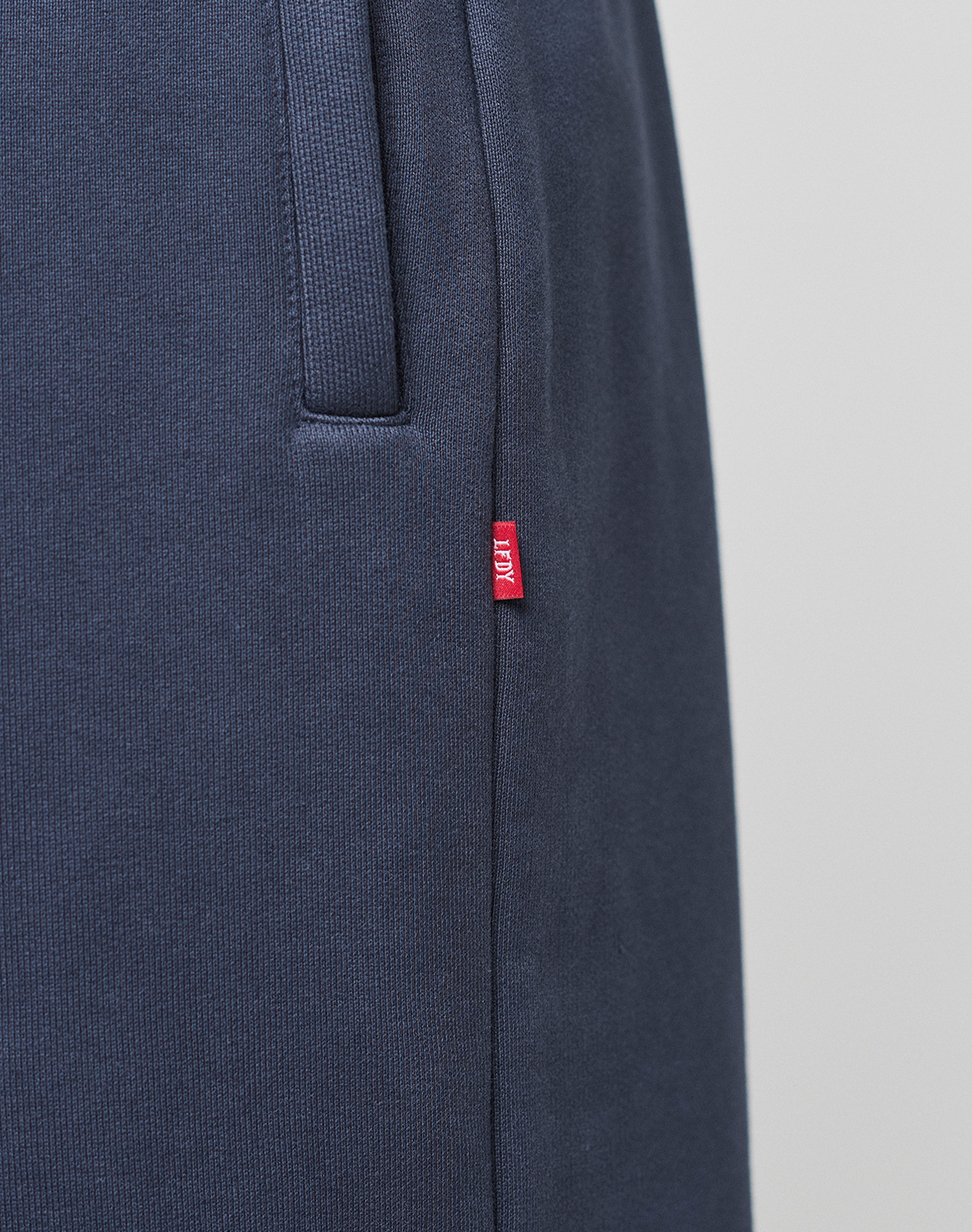 Close-up of navy blue LFDY Heavyweight Loungepants by LIVE FAST DIE YOUNG in 100% cotton, featuring a ribbed waistband, side pocket, and a small red fabric tag with white text on the side seam.