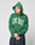 A person in a LIVE FAST DIE YOUNG Live Fast College Hooded green oversize hoodie with front print stands with eyes closed and hands clasped against a plain light background.