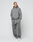 A person stands against a plain background wearing LIVE FAST DIE YOUNG’s Basic Wide Jogger in grey, paired with an oversized zip-up hoodie and white sneakers. Their hands are in their pockets and their expression is neutral.