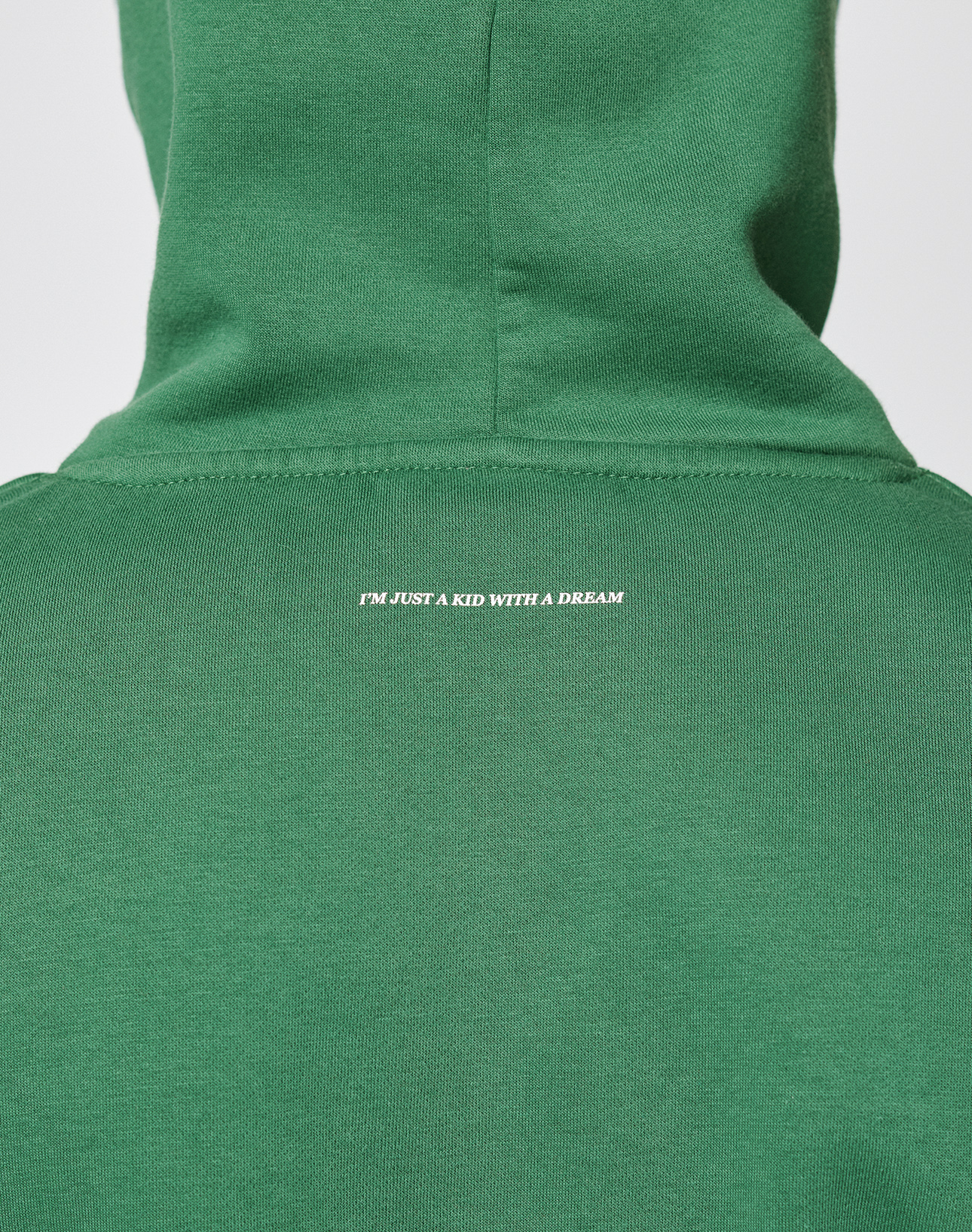 A close-up of the back of the Live Fast College Hooded by LIVE FAST DIE YOUNG in green, featuring small white "IM JUST A KID WITH A DREAM" text on top. Made from a soft Baumwolle polyester blend for lasting comfort; shown with hood up and oversize fit.