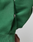 Close-up of a green Live Fast College Hooded by LIVE FAST DIE YOUNG, with a small black ACTV tag on the side seam near the pocket. Part of an arm is visible against a plain, light-colored background.