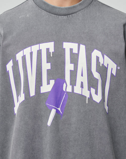 A person wears the Live Fast Ice Tee by LIVE FAST DIE YOUNG—an oversize fit gray shirt with a white and purple LIVE FAST front print and a purple popsicle illustration, made from 100% Baumwolle.