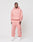 A man stands against a white background wearing a light pink LIVE FAST DIE YOUNG Loose Fit hoodie and matching Loose Jogger sweatpants with an elastic waistband, both made from soft cotton. He looks slightly to the side with his hands relaxed by his sides.