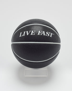 The Live Fast Basketball by LIVE FAST DIE YOUNG features a black design with white stripes, deep grooves, and LIVE FAST branding in hygroscopic PU, displayed on a clear stand against a white background.