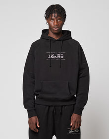 A man with short, textured hair wears a black LFDY Embroidery Hooded hoodie and matching sweatpants by LIVE FAST DIE YOUNG, both with white Clive Rest logos. He stands against a plain light gray background, looking directly at the camera. | model