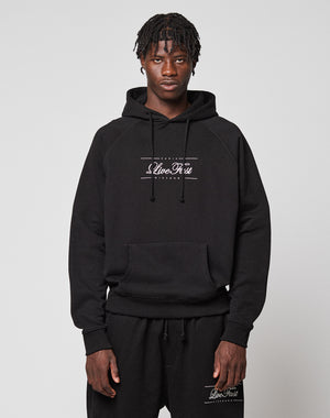 A man with short, textured hair wears a black LFDY Embroidery Hooded hoodie and matching sweatpants by LIVE FAST DIE YOUNG, both with white Clive Rest logos. He stands against a plain light gray background, looking directly at the camera.