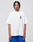 A man with braided hair wears the LIVE FAST DIE YOUNG Live Fast Lenox Tee, an oversized white cotton T-shirt with blue front print, paired with matching blue shorts. He stands facing forward against a plain light gray background.