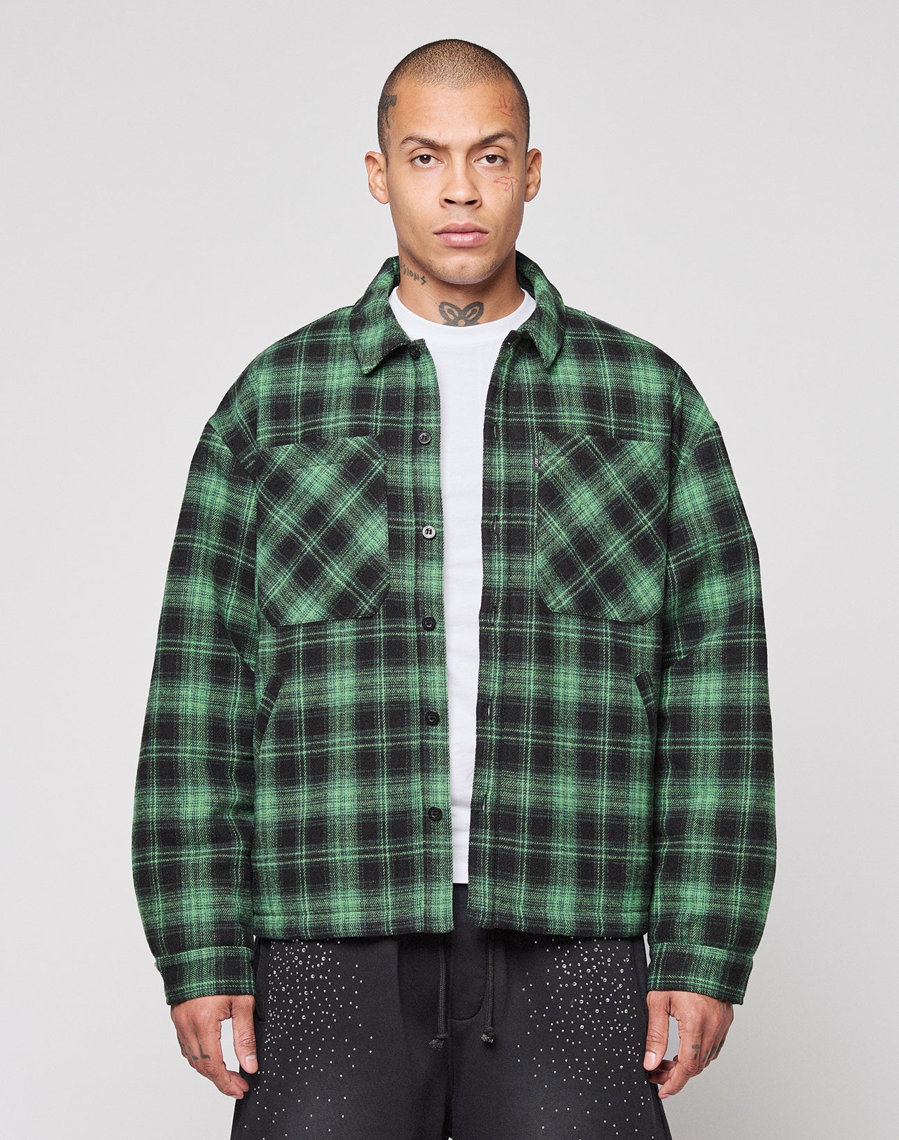 A person wearing a green and black LIVE FAST DIE YOUNG LFDY Padded Flannel over a white shirt stands facing forward against a plain light background.