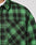 Close-up of the green and black LFDY Padded Flannel Overshirt by LIVE FAST DIE YOUNG, featuring Brusttaschen and a small tag. Worn over a white T-shirt, only part of the wearer’s neck and shoulder is visible.