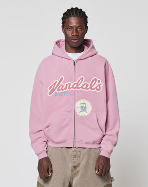 A man faces the camera in a neutral pose, wearing the LIVE FAST DIE YOUNG LFDY Vandals Hooded Zip in light pink with a “Vandals Metro” front print, paired with beige pants, against a plain background.
