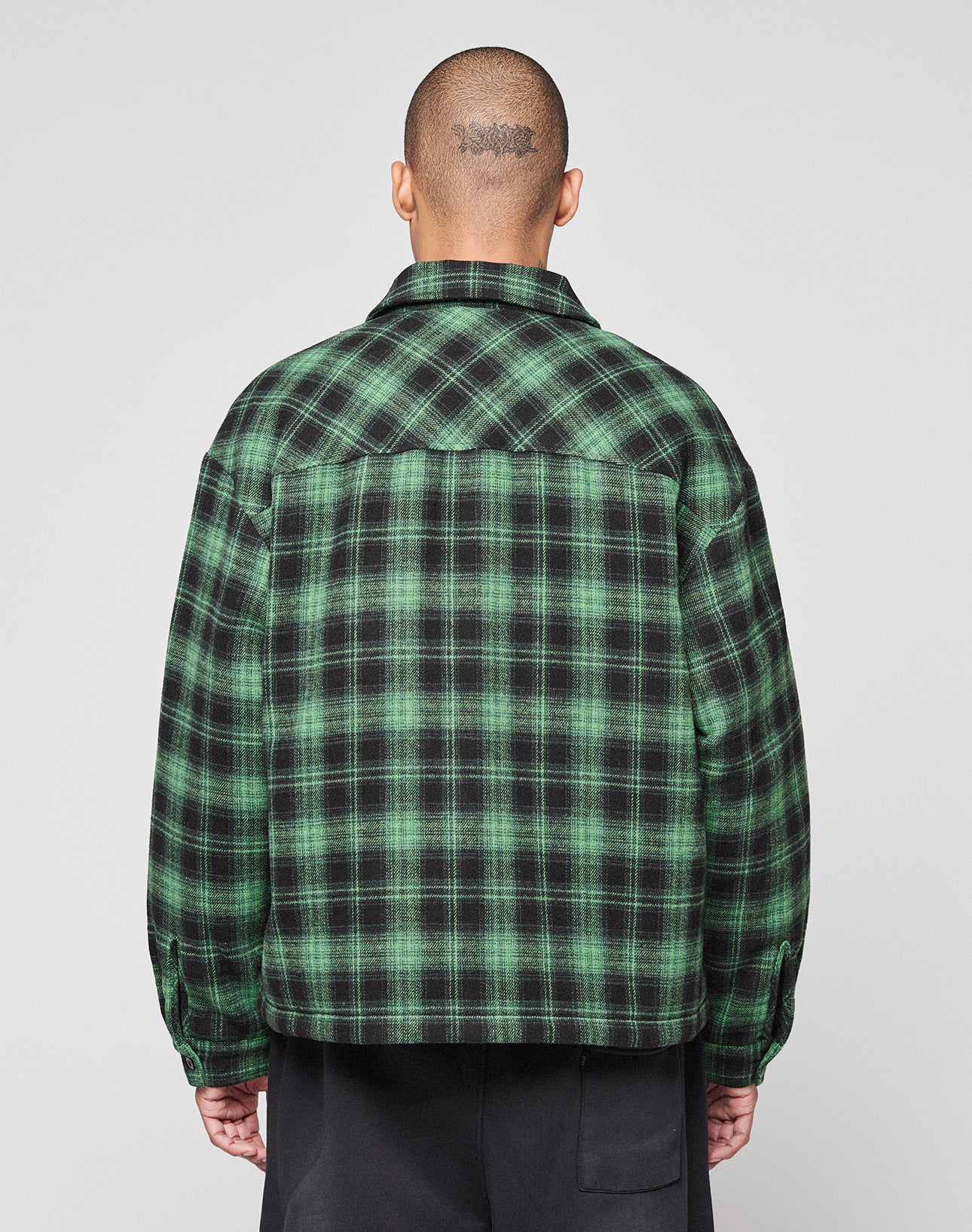 A person with a shaved head and a visible tattoo on the back of their head is seen from behind, wearing the green and black LFDY Padded Flannel by LIVE FAST DIE YOUNG against a plain light background.