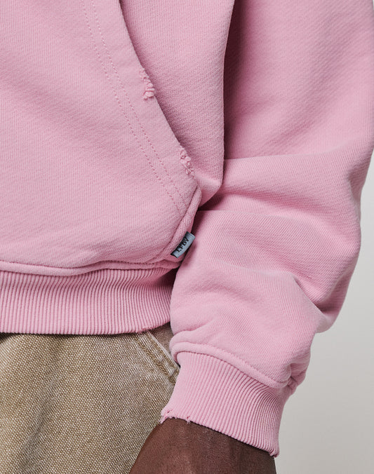 A close-up of a person wearing the LFDY Vandals Hooded Zip by LIVE FAST DIE YOUNG in light pink Oversize Fit, featuring ribbed cuffs and hem, paired with beige pants. The image highlights the sleeve and side seam details.