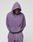 A person wearing the LIVE FAST DIE YOUNG Basic Evidence Hooded oversize purple cotton-polyester sweatshirt and matching sweatpants stands against a plain light background, hood up, looking down with hands behind their back.