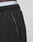 Close-up of a person wearing LIVE FAST DIE YOUNG LFDY Dealership Trackpants in black, featuring a wide fit, exposed gold zipper pocket, and white underwear waistband visible above the elastic waistband.