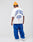 A person in an Oversize Fit white LIVE FAST DIE YOUNG Live Fast Lenox Tee with bold blue front and back LIVE FAST print and blue sweatpants stands facing away from the camera against a plain white background.