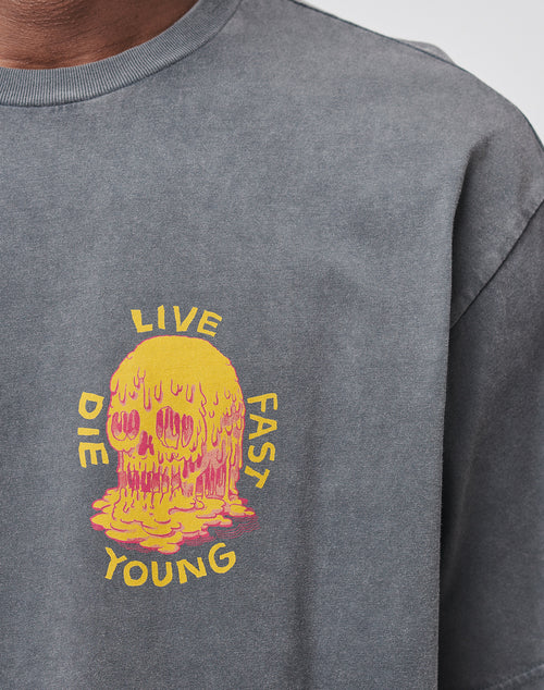 Someone wearing the Melting Chest Tee by LIVE FAST DIE YOUNG—a gray vintage-wash t-shirt with a melting yellow and pink skull graphic and “LIVE FAST DIE YOUNG” text.