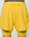 A person wears LIVE FAST DIE YOUNG Live Fast Performance Running Shorts in bright yellow, featuring lightweight fabric, a zippered back pocket, and integrated tights with LIVE and FAST printed in gray near each hem.